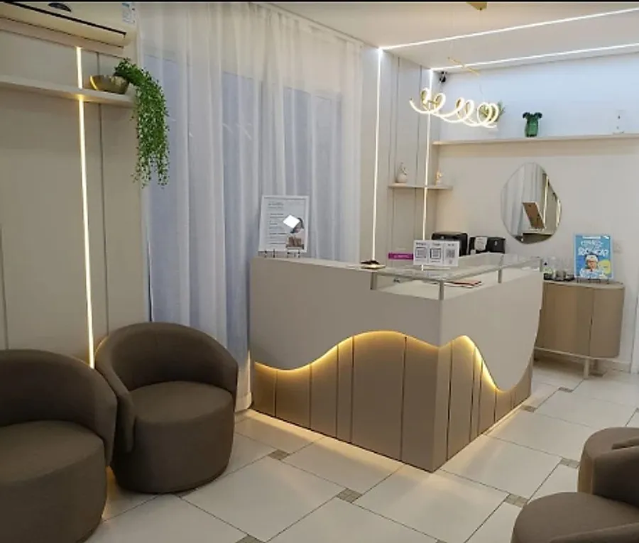 Recepção da Prime Odontologia, com o balcão iluminado, poltronas e cortinas claras