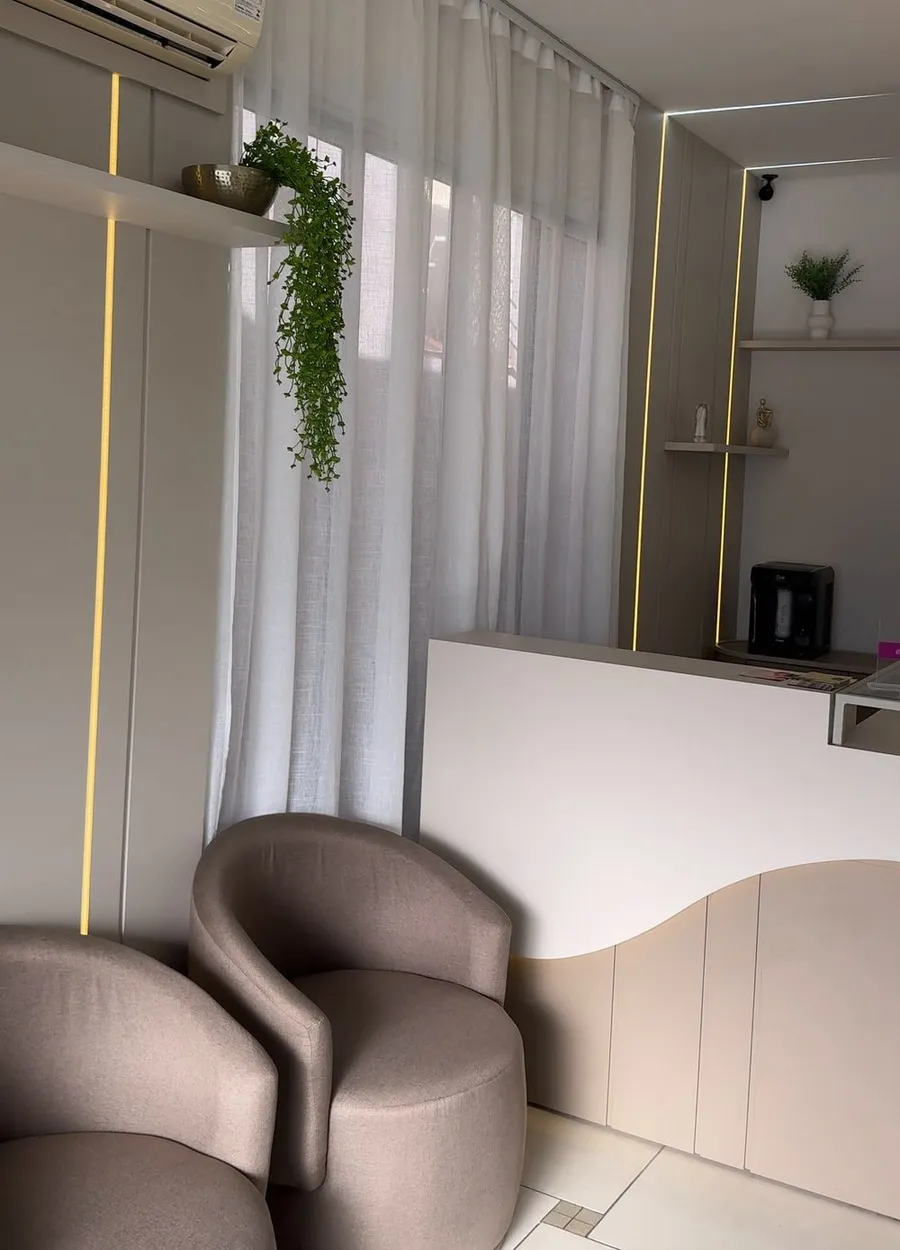 Sala de espera com poltronas, cortinas claras e faixas de luz nas paredes